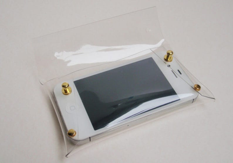 May include: A clear plastic phone case with gold metal snaps. A white smartphone is inside the case.