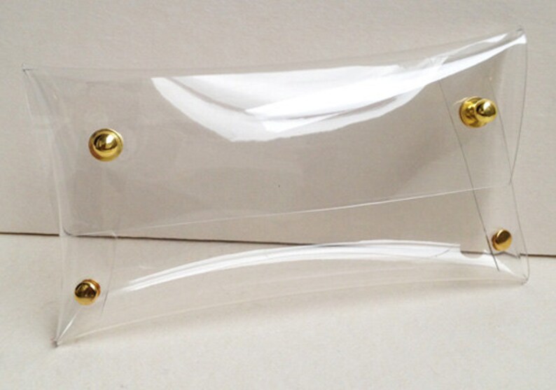 May include: A clear plastic clutch bag with gold metal accents. The bag has a flap closure and a smooth, shiny finish.