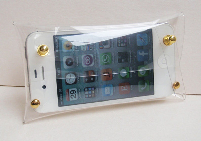 May include: A clear plastic phone case with gold accents. The case has a flap that folds over the top of the phone. A white smartphone is inside the case. The phone screen shows a variety of app icons.