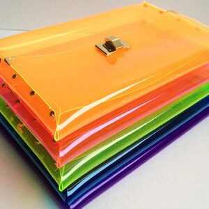 May include: A stack of six clear plastic clutch bags in rainbow colors, with a gold clasp on the top bag.
