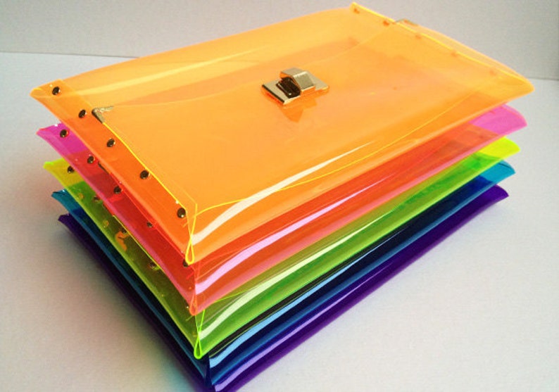 May include: A stack of six clear plastic clutch bags in rainbow colors, with a gold clasp on the top bag.
