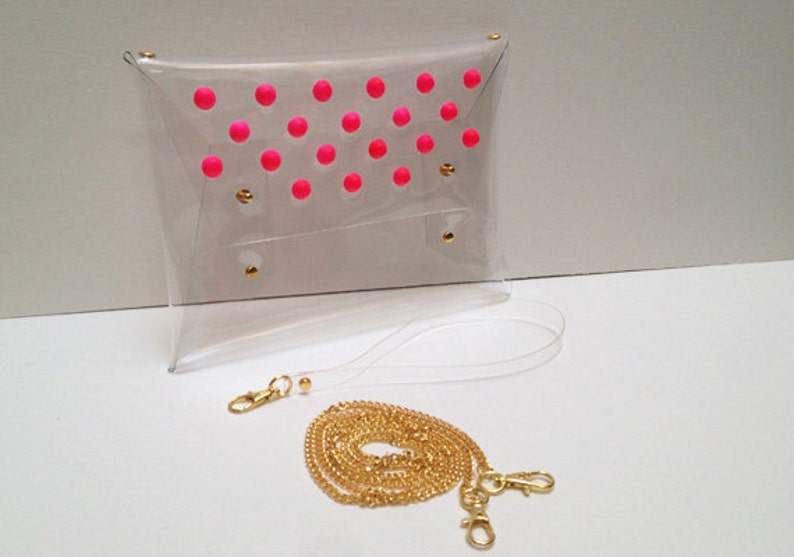 Puede incluir: Un bolso de mano transparente de pl&aacute;stico con un dise&ntilde;o de lunares rosas y una correa de cadena dorada.