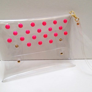 Puede incluir: Una cartera de mano transparente de pl&aacute;stico con un dise&ntilde;o de lunares rosas y una correa de cadena dorada.
