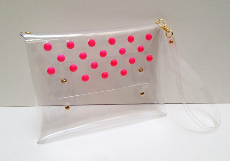 Puede incluir: Una cartera de mano transparente de pl&aacute;stico con un dise&ntilde;o de lunares rosas y una correa de cadena dorada.