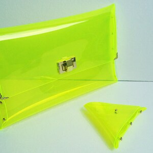 May include: A bright neon yellow plastic clutch purse with a gold clasp and a matching smaller triangular pouch.