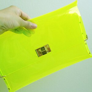 May include: A bright neon yellow clutch purse with a gold clasp.