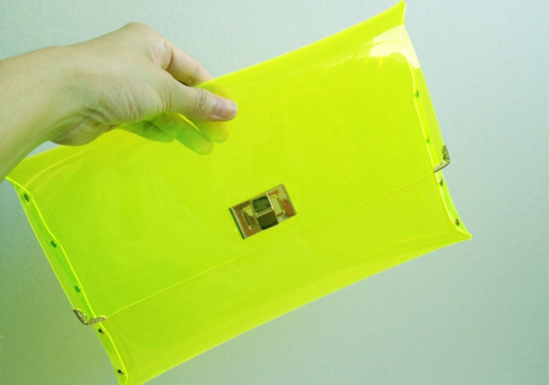 May include: A bright neon yellow clutch purse with a gold clasp.