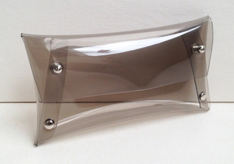 May include: A clear plastic clutch bag with a brown tint and silver metal clasps.