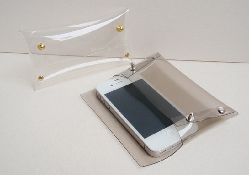 May include: A clear plastic clutch with silver snaps and a white smartphone inside. The clutch is slightly translucent, showing the phone through the plastic.
