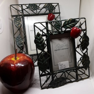 May include: Two black metal picture frames with a green vine and leaf design. The frames are empty and have a red apple accent. The text on the frame reads "Bairnes FRAME-A-MEMORY" and "EC Apple Home $5.50".