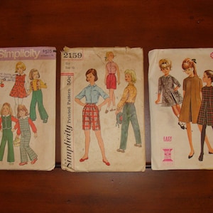 May include: Three vintage sewing patterns for girls' clothing. The Simplicity patterns are for a child's dress and a girl's pants. The McCall's pattern is for a girl's dress. The patterns are printed on paper and have illustrations of the garments.