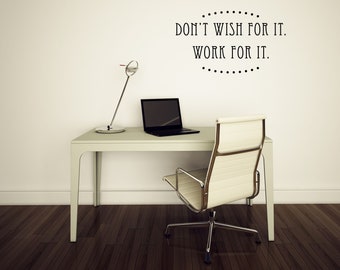 May include: A modern office setup featuring a white desk, a black laptop, and a silver desk lamp. A cream-colored office chair sits in front of the desk. The wall displays the text "DON'T WISH FOR IT. WORK FOR IT."
