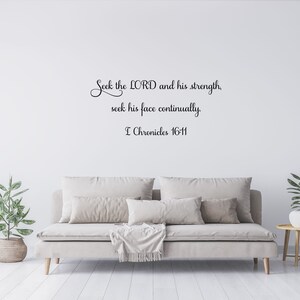 May include: A white wall with a black cursive quote that reads "Seek the LORD and his strength, seek his face continually. I Chronicles 16-11". The quote is displayed above a light beige sofa with a throw blanket and pillows. A small potted plant is on the left side of the sofa and a small table with a potted plant is on the right side of the sofa.