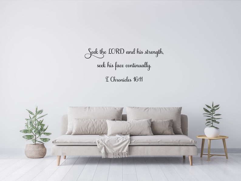 May include: A white wall with a black cursive quote that reads "Seek the LORD and his strength, seek his face continually. I Chronicles 16-11". The quote is displayed above a light beige sofa with a throw blanket and pillows. A small potted plant is on the left side of the sofa and a small table with a potted plant is on the right side of the sofa.