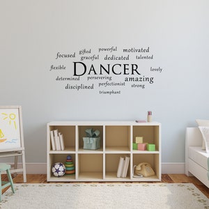 May include: A white wall with a black vinyl decal that reads "DANCER" surrounded by positive words describing a dancer. The decal is in a child's bedroom with a white bookshelf, a white easel with a drawing of a boat and sun, a green stool, and a white bed with a blue blanket.