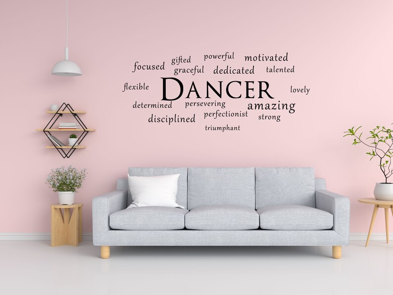 May include: A pink wall with a grey sofa and a word art decal that says "DANCER" with a list of positive words describing a dancer, such as "gifted", "powerful", "motivated", "focused", "graceful", "dedicated", "talented", "flexible", "determined", "persevering", "amazing", "disciplined", "perfectionist", "strong", "lovely", and "triumphant".