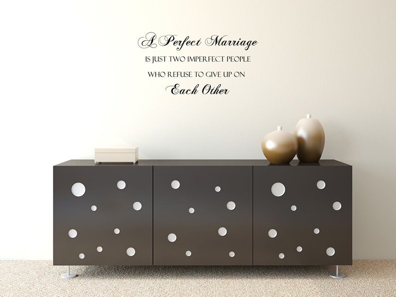 May include: A black and white wall decal with the quote "A Perfect Marriage is just two imperfect people who refuse to give up on Each Other". The decal is displayed on a white wall above a black dresser with white polka dots.