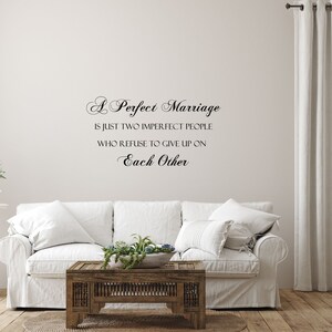 May include: A white couch with pillows in a living room setting. The wall behind the couch has a black vinyl decal with the text "A Perfect Marriage is just two imperfect people who refuse to give up on Each Other."