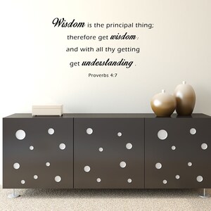 May include: A black and white wall decal with the quote "Wisdom is the principal thing; therefore get wisdom: and with all thy getting get understanding. Proverbs 4:7". The decal is displayed on a white wall above a dark brown dresser with white circles.