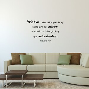 May include: A white wall with a black and white quote from Proverbs 4:7 that reads "Wisdom is the principal thing; therefore get wisdom. and with all thy getting get understanding." The quote is displayed on a white wall in a living room setting with a white couch and a brown coffee table.
