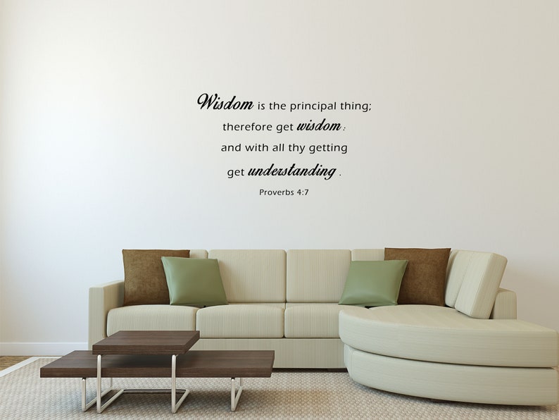 May include: A white wall with a black and white quote from Proverbs 4:7 that reads "Wisdom is the principal thing; therefore get wisdom. and with all thy getting get understanding." The quote is displayed on a white wall in a living room setting with a white couch and a brown coffee table.