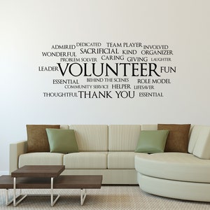 May include: A white wall with a black vinyl decal that reads "ADMIRED DEDICATED TEAM PLAYER INVOLVED SACRIFICIAL KIND ORGANIZER PROBLEM SOLVER CARING GIVING LAUGHTER WONDERFUL LEADER VOLUNTEER FUN ESSENTIAL BEHIND THE SCENES ROLE MODEL COMMUNITY SERVICE HELPER LIFESAVER THOUGHTFUL THANK YOU ESSENTIAL". The decal is above a white couch with green and brown throw pillows. The couch is in front of a white wall.