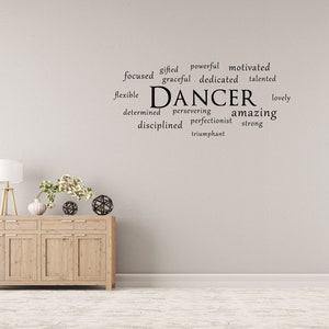 May include: A white wall with a black word cloud that reads "gifted powerful motivated focused graceful dedicated talented flexible DANCER lovely determined persevering amazing disciplined perfectionist strong triumphant". A wooden dresser with three drawers and four doors is in the foreground.