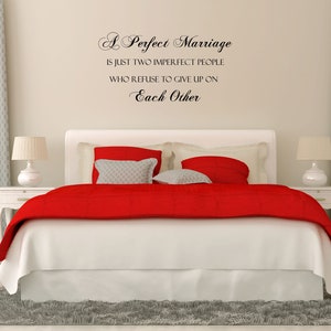 May include: A white bedroom with a red and white bed, a gray rug, and a quote on the wall that reads "A Perfect Marriage is just two imperfect people who refuse to give up on Each Other."