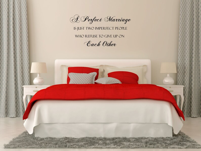 May include: A white bedroom with a red and white bed, a gray rug, and a quote on the wall that reads "A Perfect Marriage is just two imperfect people who refuse to give up on Each Other."