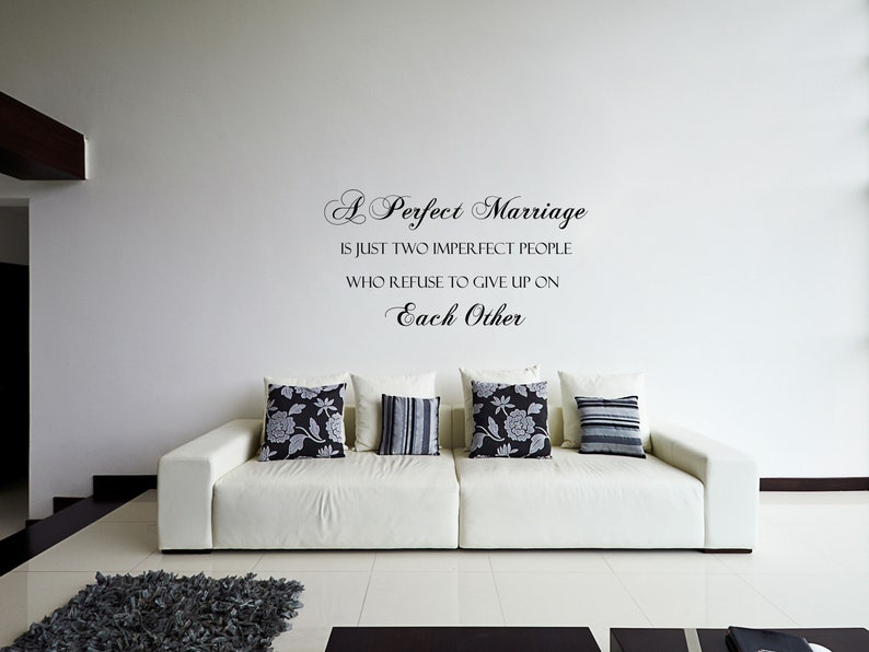 May include: A white couch with black and white patterned throw pillows in a living room with a white wall and a quote that reads "A Perfect Marriage is just two imperfect people who refuse to give up on each other."