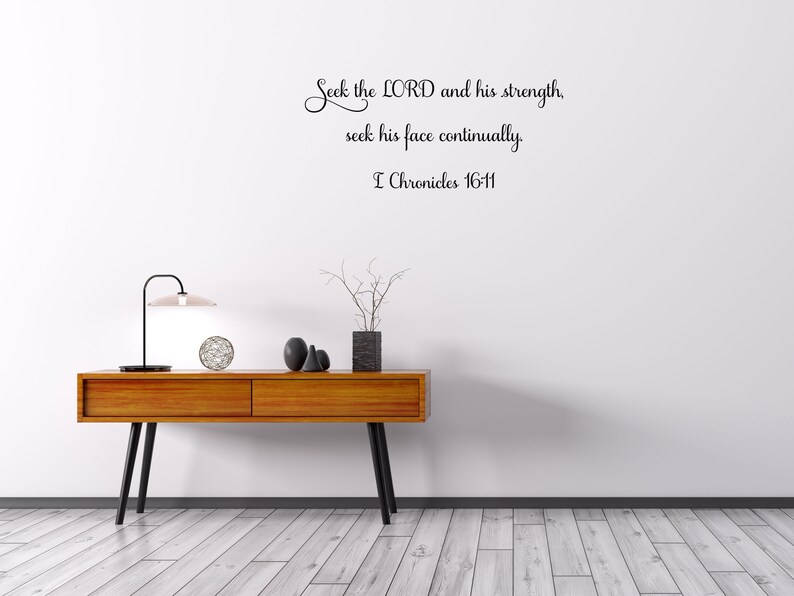 May include: A white wall with a black cursive quote that reads "Seek the LORD and his strength, seek his face continually. I Chronicles 16-11". The wall is decorated with a wooden table, a lamp, and a vase with branches.