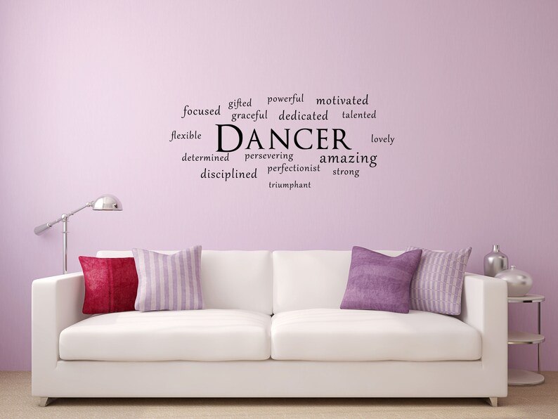 May include: A white sofa with two cushions, one purple and one striped, in a room with a light purple wall. The wall has a black word art decal that says "DANCER" surrounded by words describing the qualities of a dancer, such as "gifted", "powerful", "motivated", "graceful", "dedicated", "talented", "flexible", "determined", "persevering", "amazing", "disciplined", "perfectionist", "strong", "lovely", and "triumphant".