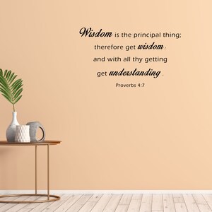 May include: A beige wall with a quote from Proverbs 4:7, "Wisdom is the principal thing; therefore get wisdom: and with all thy getting get understanding." The quote is written in black cursive font. A small table with a vase and two decorative items sits in front of the wall.