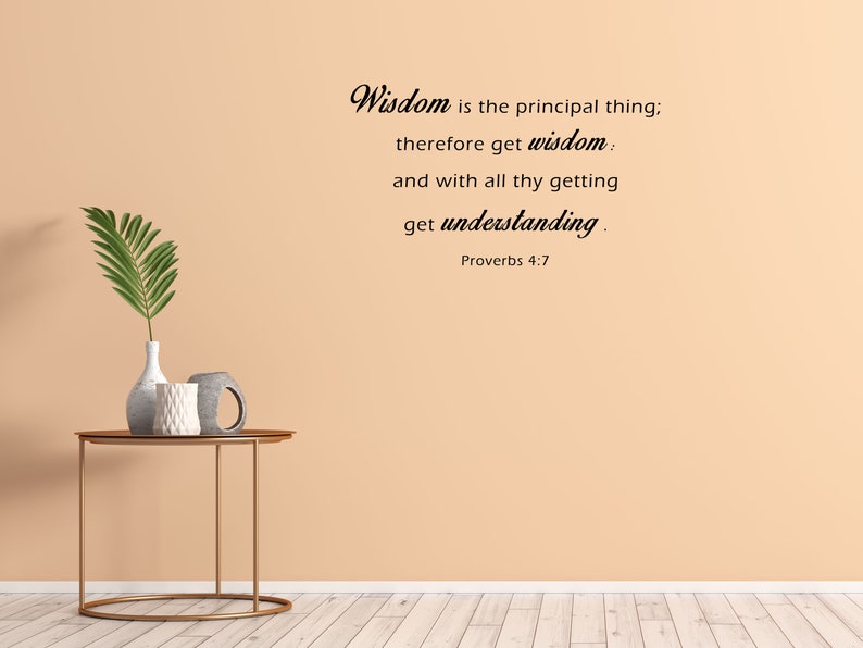 May include: A beige wall with a quote from Proverbs 4:7, "Wisdom is the principal thing; therefore get wisdom: and with all thy getting get understanding." The quote is written in black cursive font. A small table with a vase and two decorative items sits in front of the wall.