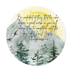 Op de afbeelding: Rond aquarelontwerp met een berglandschap met dennen, vogels en een gele zon. De tekst luidt: "Wees ervan overtuigd dat Hij die in u een goed werk begonnen is, het ook zal voltooien tot de dag van Christus Jezus Filippenzen 1:6."