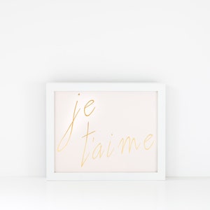 Puede incluir: Marco de imagen blanco con fondo rosa claro y letras doradas que dicen "je t'aime".