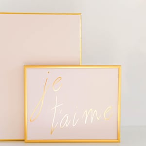 Puede incluir: Dos cuadros con marco dorado y fondo rosa claro. El cuadro m&aacute;s peque&ntilde;o tiene el texto "je t'aime" escrito en letras doradas.