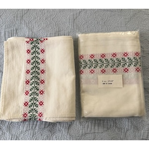 Könnte beinhalten: Zwei cremefarbene Baumwolltücher mit gestickten Blumenmustern in Grün und Rot. Ein Tuch ist gefaltet, das andere in einer transparenten Kunststoffverpackung. Die Verpackung hat ein Etikett mit der Aufschrift "6 pcs 25.4cm x 25.4cm 100% Cotton."