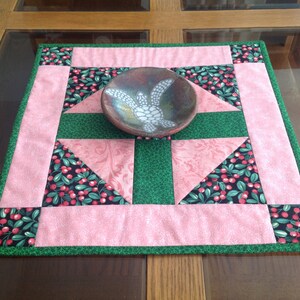 May include: A pink and green quilted table runner with a white ceramic bowl featuring a turtle design in the center.