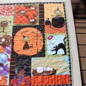 May include: A colorful Halloween-themed quilt with various characters and designs. The quilt features a witch, cats, bats, and other spooky creatures. The quilt is made of different fabrics and has a patchwork design.