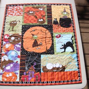 May include: A Halloween-themed quilt with a patchwork design featuring various characters and images, including a witch, a cat, and a pumpkin. The quilt is made of colorful fabrics and has a black and white border.