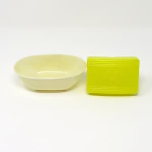 May include: A small, oval-shaped, white ceramic bowl and a bright yellow rectangular soap dish.