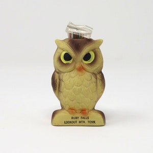 May include: A brown and yellow owl figurine with large black eyes and a clear plastic container on top. The base of the figurine reads "Ruby Falls Lookout Mtn. Tenn."
