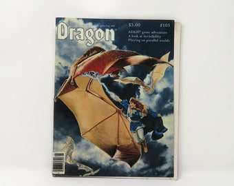 Può includere: La copertina della rivista Dragon, numero 105, mostra una donna che cavalca una creatura alata. Indossa un abito blu e bianco e lo sfondo è un cielo nuvoloso. Il testo sulla copertina della rivista dice "Dragon" e "3,00 € #105".