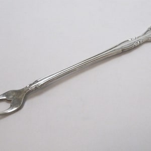 May include: A silver-toned, ornate, two-pronged fork with a decorative handle.