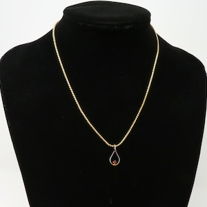 May include: A gold chain necklace with a teardrop-shaped pendant featuring a red gemstone.
