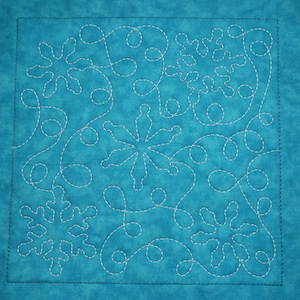 May include: A turquoise blue fabric square with a white free motion quilting design of snowflakes and swirls.