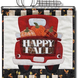 May include: A red truck with a white tailgate carrying a load of pumpkins. The truck is on a black and white checkered background with a wooden fence in the foreground. The text "HAPPY FALL" is printed on the tailgate.