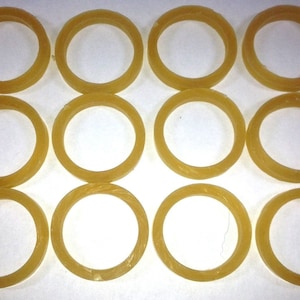 May include: Twelve rubber bands in a light brown color, arranged in four rows of three. The rubber bands are all the same size and shape, and they are all lying flat on a white surface.