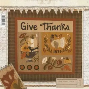 May include: A brown and tan patchwork quilt block with the words "Give Thanks" in the center. The block features a variety of autumnal designs, including a cornucopia, a turkey, and a pumpkin.